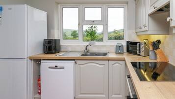 A modern kitchen with white cabinets, a built-in dishwasher, a coffee maker, a toaster, and a window with a view of greenery.