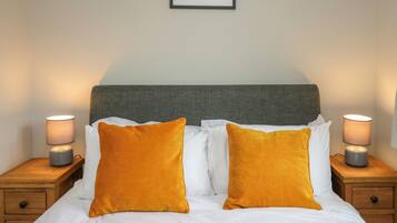 Een net opgemaakt bed met witte lakens en twee mosterdgele kussens, aan weerszijden geflankeerd door nachtkastjes met lampen, in een kamer met een lijstwerkfoto van Elan Valley aan de muur.