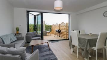 Uma sala de estar moderna com um sofá cinzento, uma mesa de centro e uma área de jantar com mesa e cadeiras.