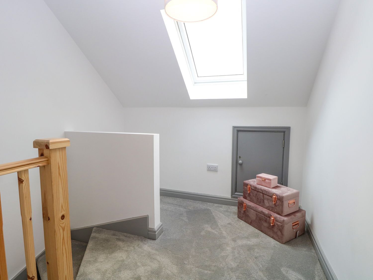 Um quarto pequeno e bem iluminado, com claraboia, guarda-corpo de madeira e uma porta, com malas encostadas na parede.