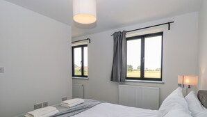 Une chambre à coucher avec un lit, deux fenêtres, un radiateur, une lampe et une serviette sur le lit.