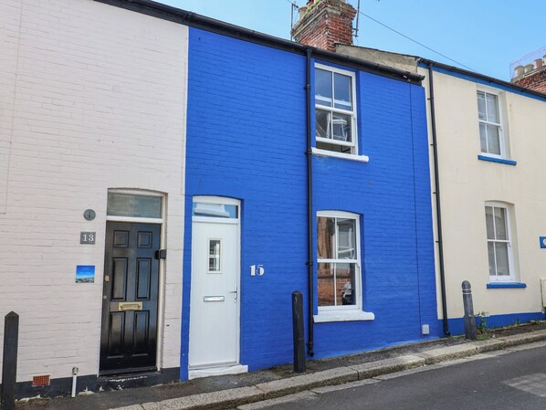 A row of terraced houses with distinct white and blue exteriors, numbered doors, and visible windows. - Mackerel Cottage (Weymouth)