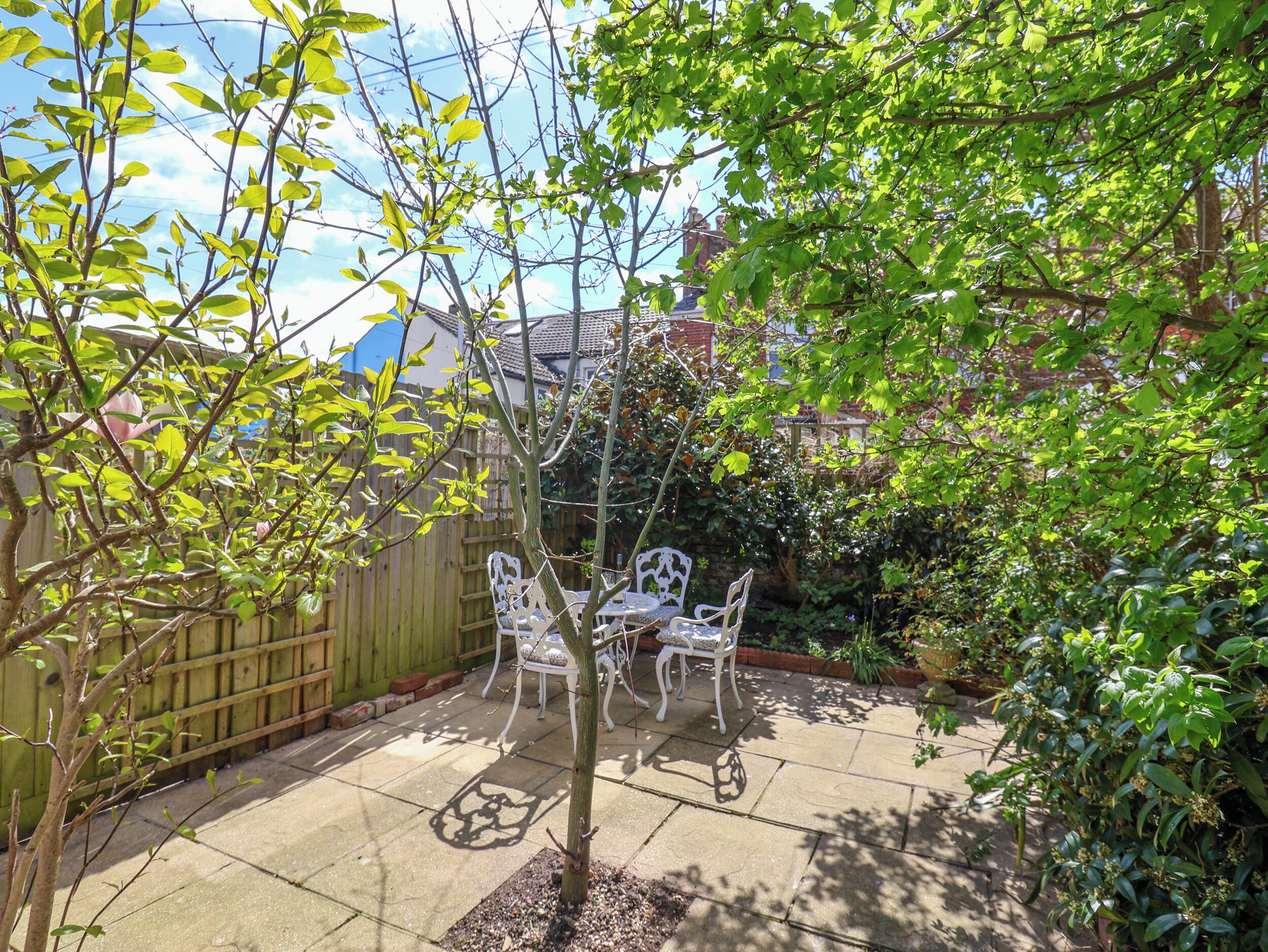 A patio with a table and chairs, surrounded by a wooden fence and greenery.