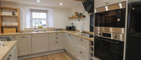 A modern kitchen with light-colored cabinets, a wooden countertop, a built-in oven, and a microwave.
