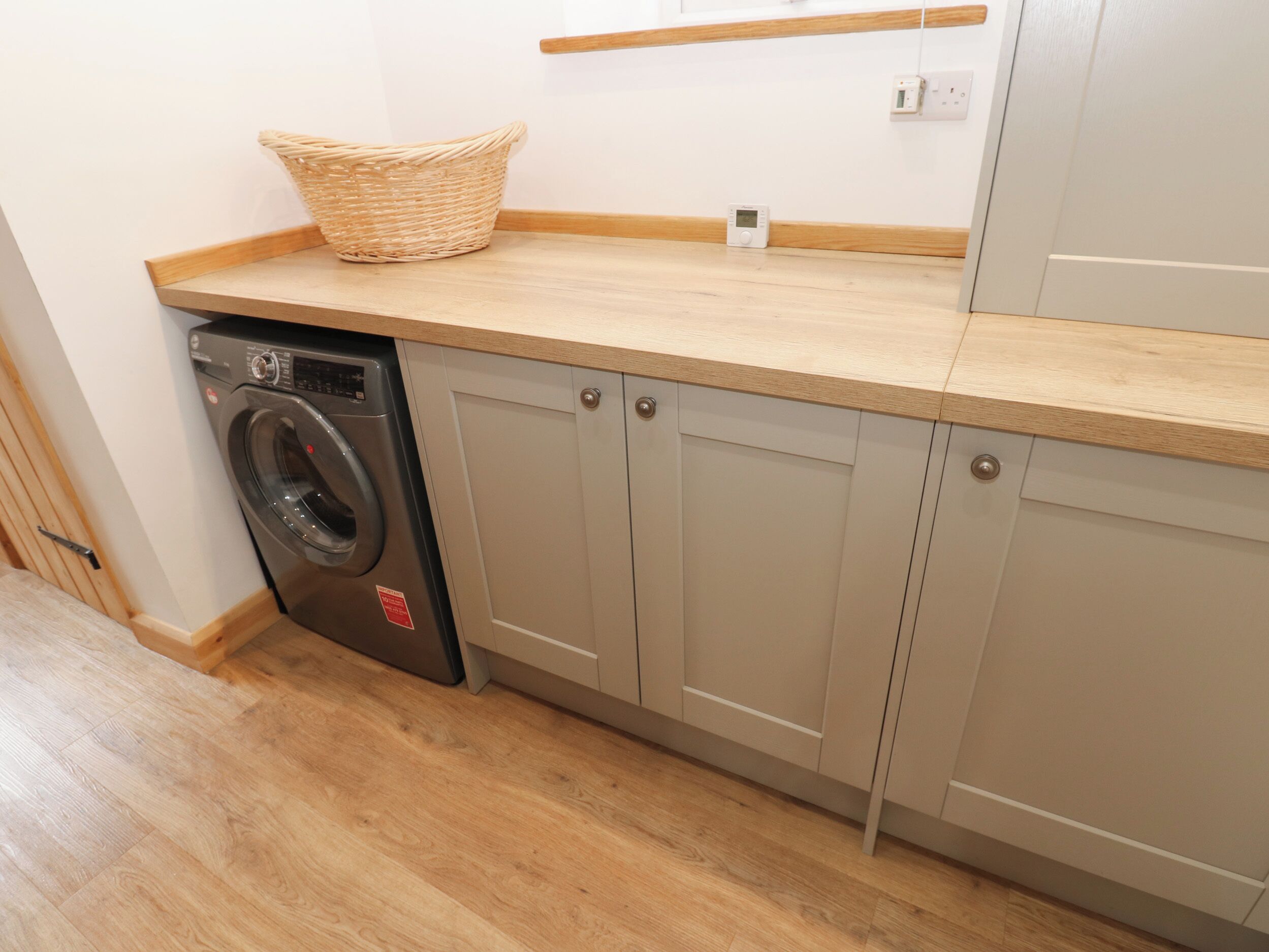 A laundry area with a washing machine, a basket, and a wooden countertop.