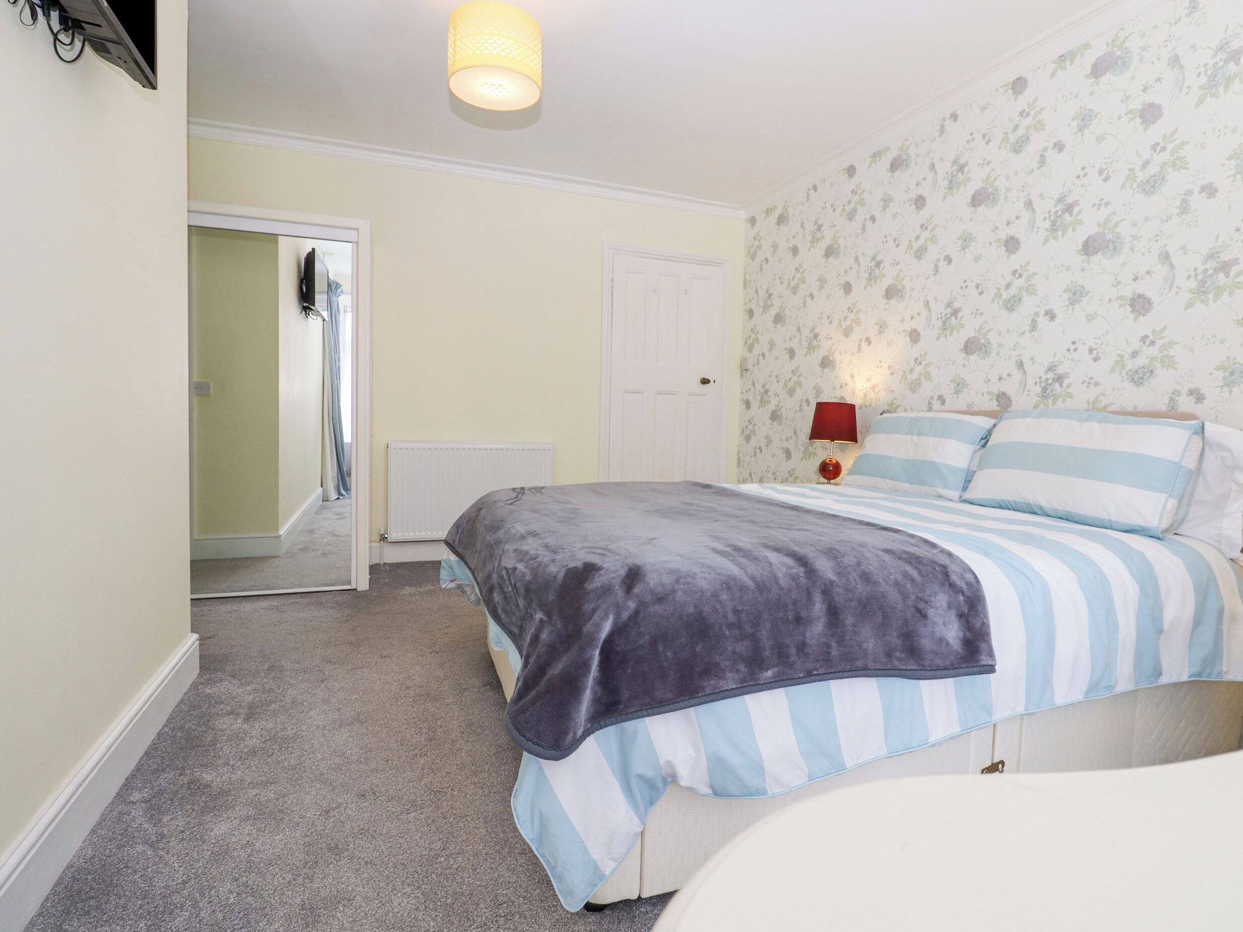 Un dormitorio con cama, radiador, puerta y pared con papel tapiz floral.