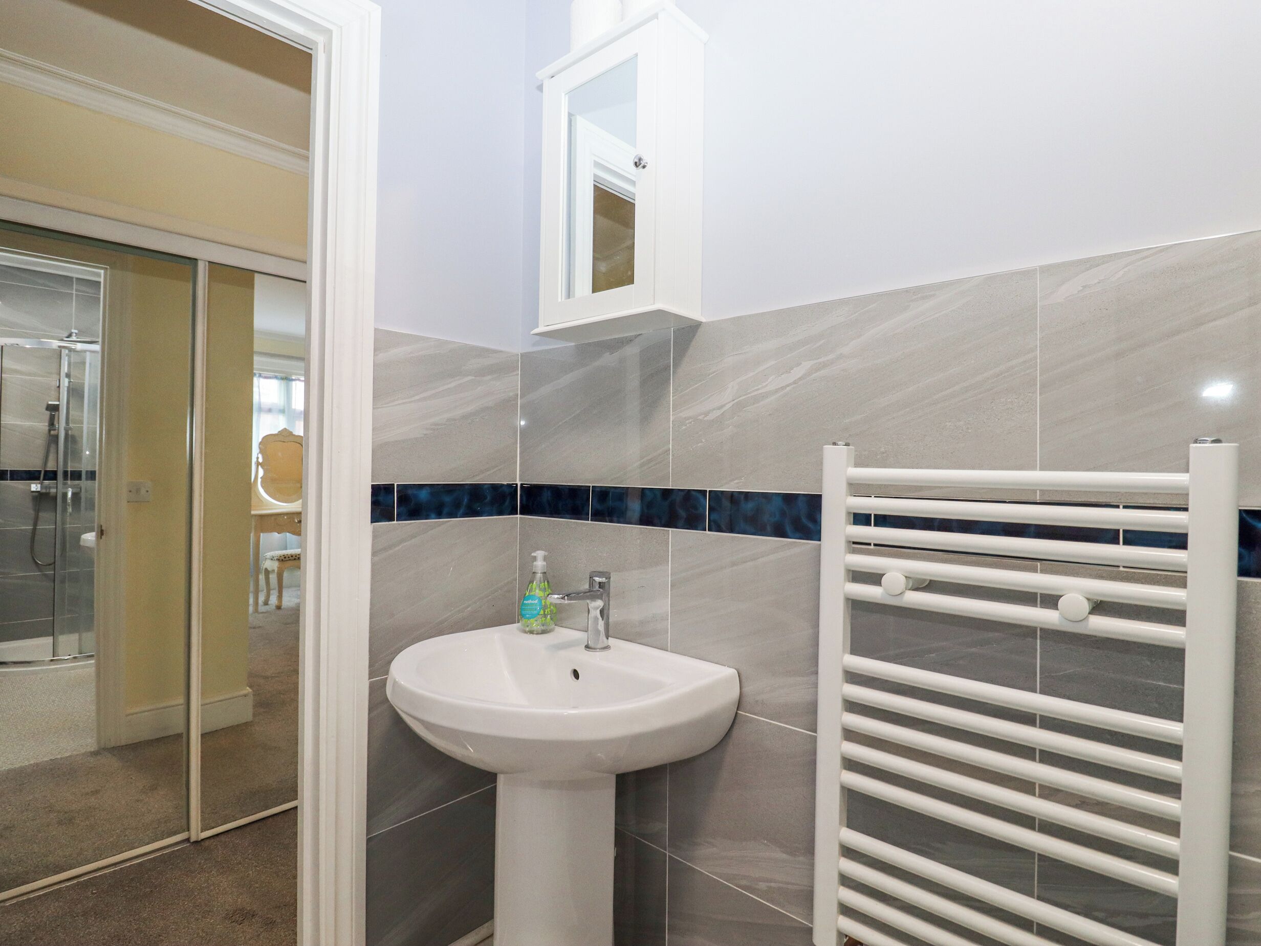 A bathroom with a white pedestal sink, a mirror above it, and a towel rack with horizontal bars.