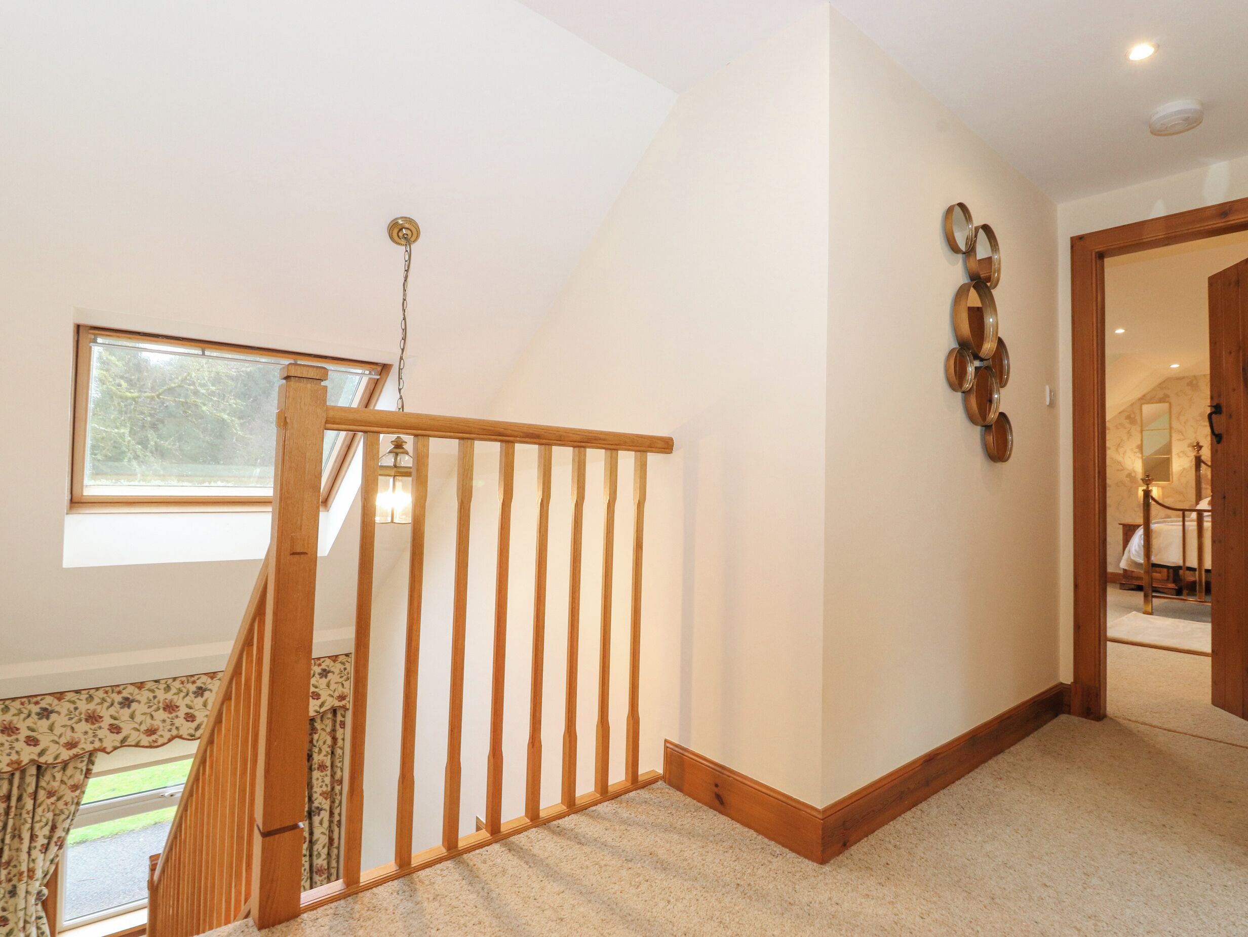 Una escalera con barandillas de madera que conduce a un rellano. Se ve una ventana con vistas a árboles desde el rellano.