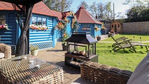 A blue wooden house with a red roof, a barbecue grill, wicker furniture, and flower baskets. - Applejacks Orchard (Holywell)