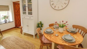 Un coin repas avec une table en bois dressée pour quatre personnes, entourée de chaises en bois. On aperçoit, au fond, un buffet blanc avec des portes en verre.