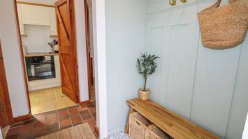 A hallway with a wooden door leading to a kitchen, a woven basket on a console table, and a wall-mounted hook with a bag.