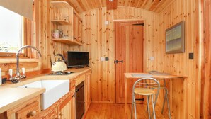 A wooden cabin interior with a kitchen area, including a sink, stove, and chair. - Hafan Gelli Sheperds Hut - Enlli (Pwllheli)