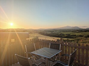 En träveranda med ett bord och stolar, med utsikt över en vacker dal och ett berg i fjärran.