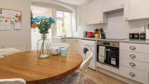A kitchen with a wooden table, white cabinets, a washing machine, and a stove. - Pendennis (Sherborne)