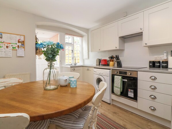 A kitchen with a wooden table, white cabinets, a washing machine, and a stove.