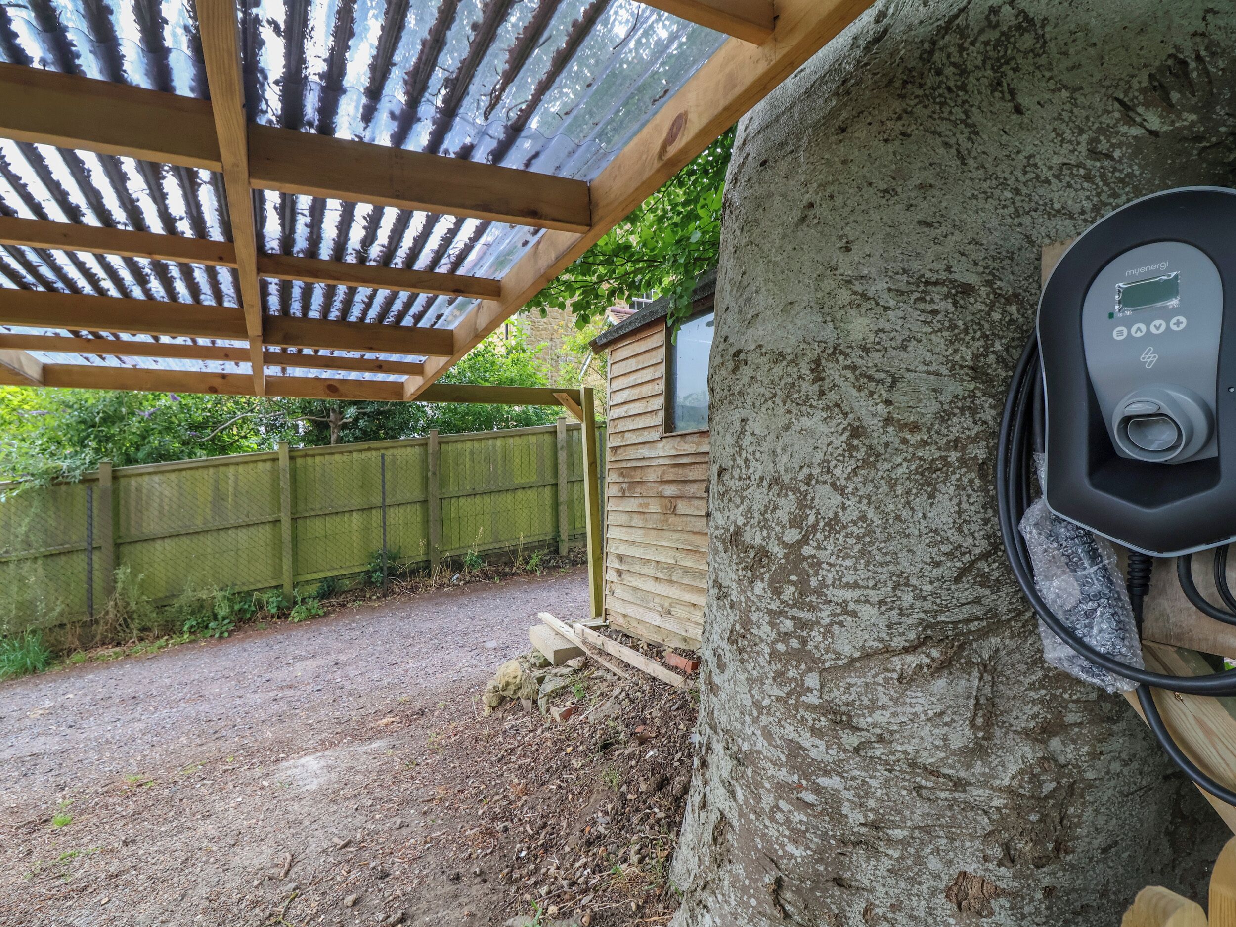 An outdoor electric vehicle charging station attached to a tree, a wooden pergola, and a wooden fence.