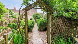 A garden pathway leading to a wooden archway, surrounded by lush greenery and a stone wall. - Pendennis (Sherborne)