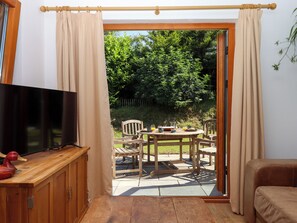 Habitación con televisor sobre un mueble de madera, una mesa con sillas y un ventanal corredizo que da a un espacio exterior con una mesa para dos.