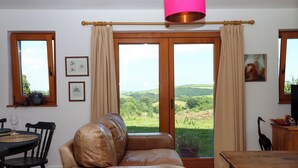 Una sala de estar con un sofá de cuero, una mesa de madera y vistas a colinas verdes a través de un amplio ventanal corredera.