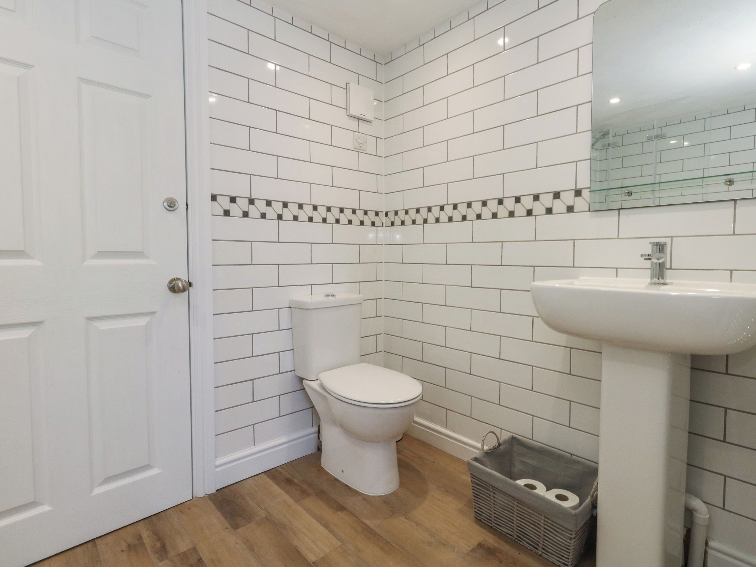 A bathroom with white subway tiles, a white toilet, a sink, and a small laundry basket.