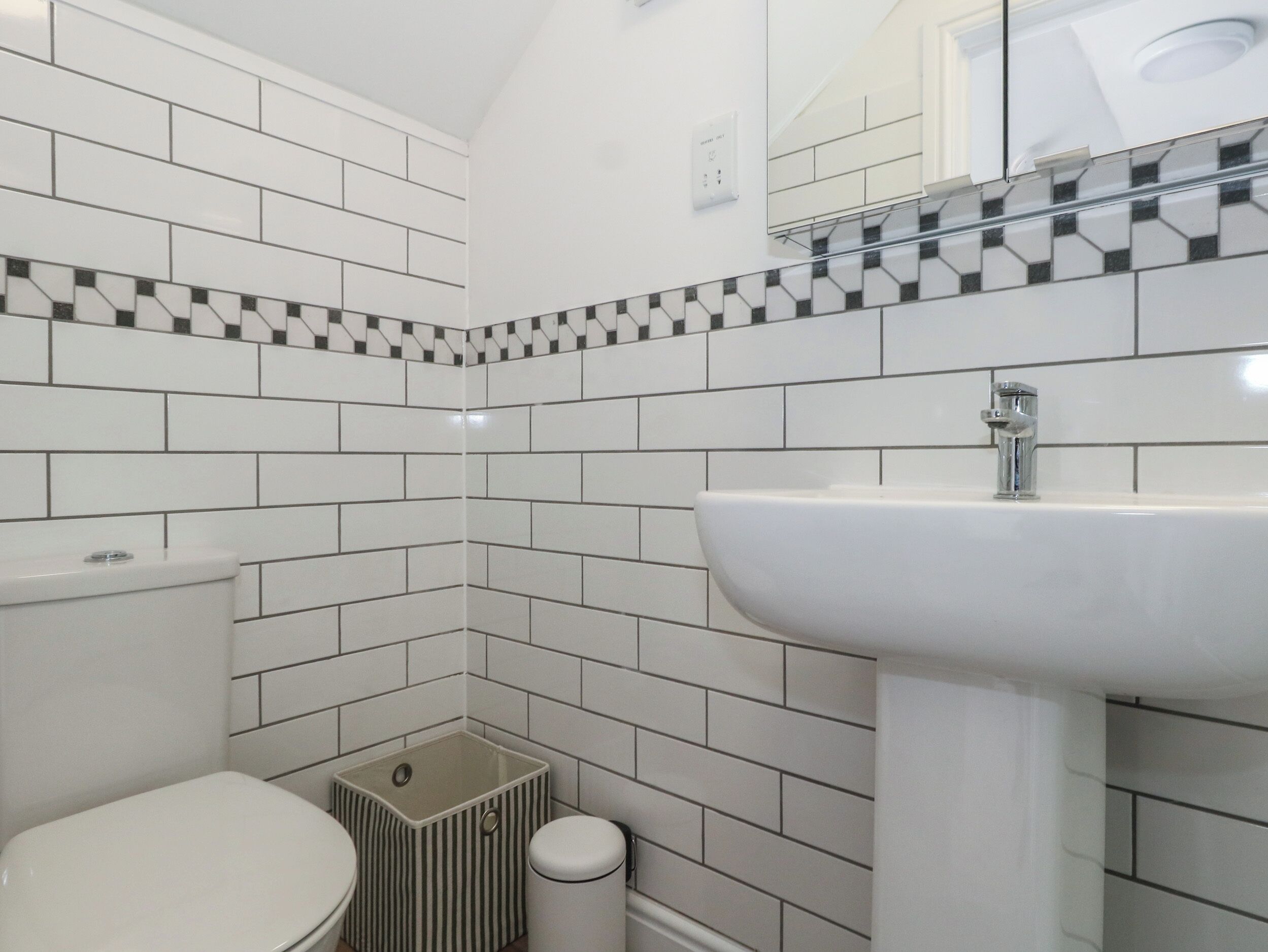 Un baño con azulejos blancos, un lavabo y un inodoro.