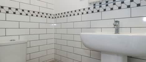 Un baño con azulejos blancos, un lavabo y un inodoro.