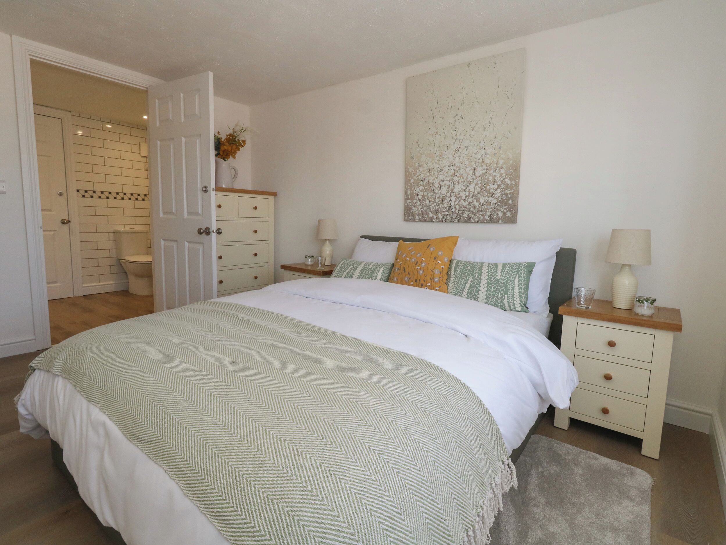 A bedroom with a bed, nightstands, a dresser, and a door leading to a bathroom.