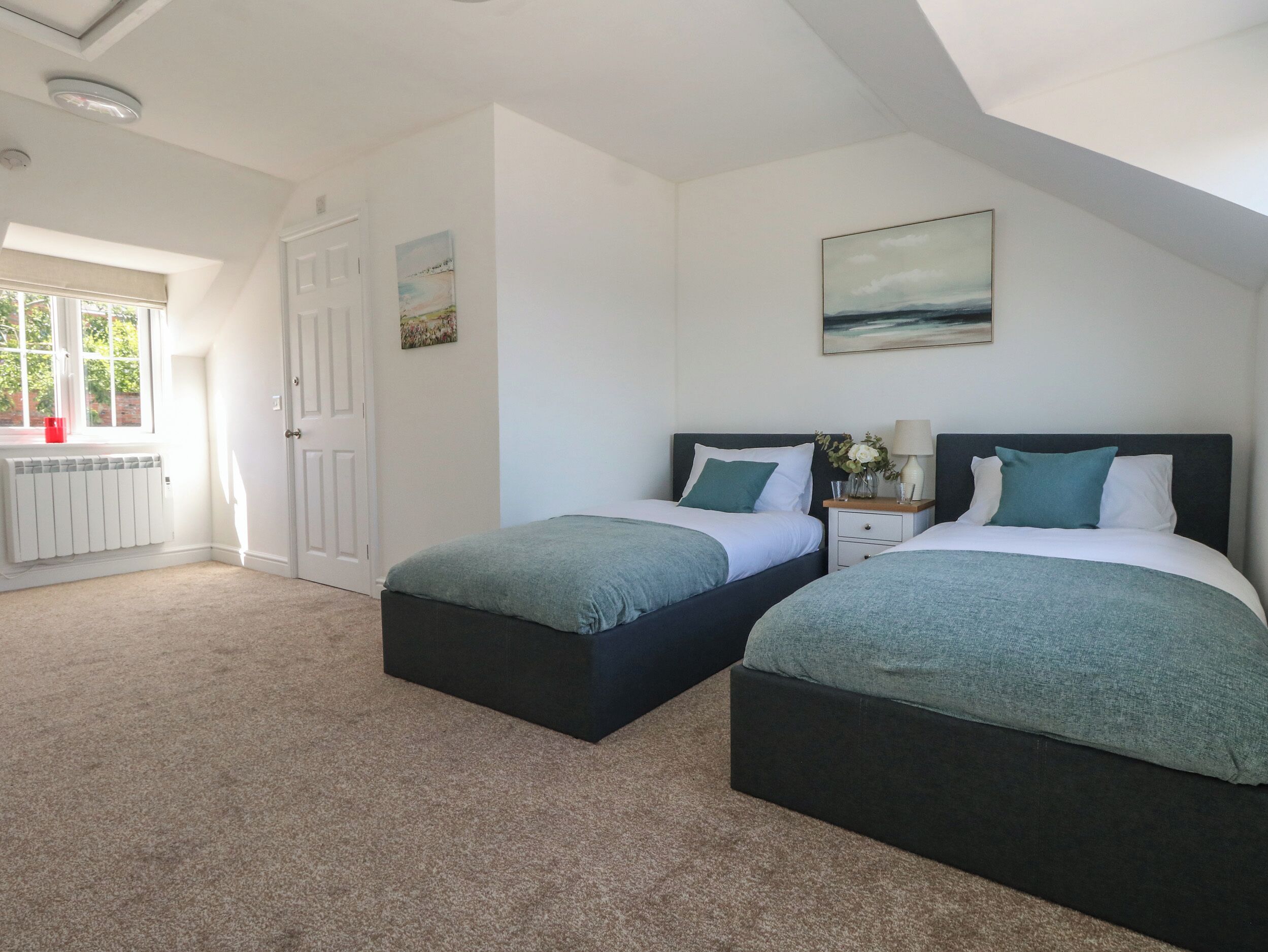 A bedroom with two beds, a radiator, a window with a view, and a door.