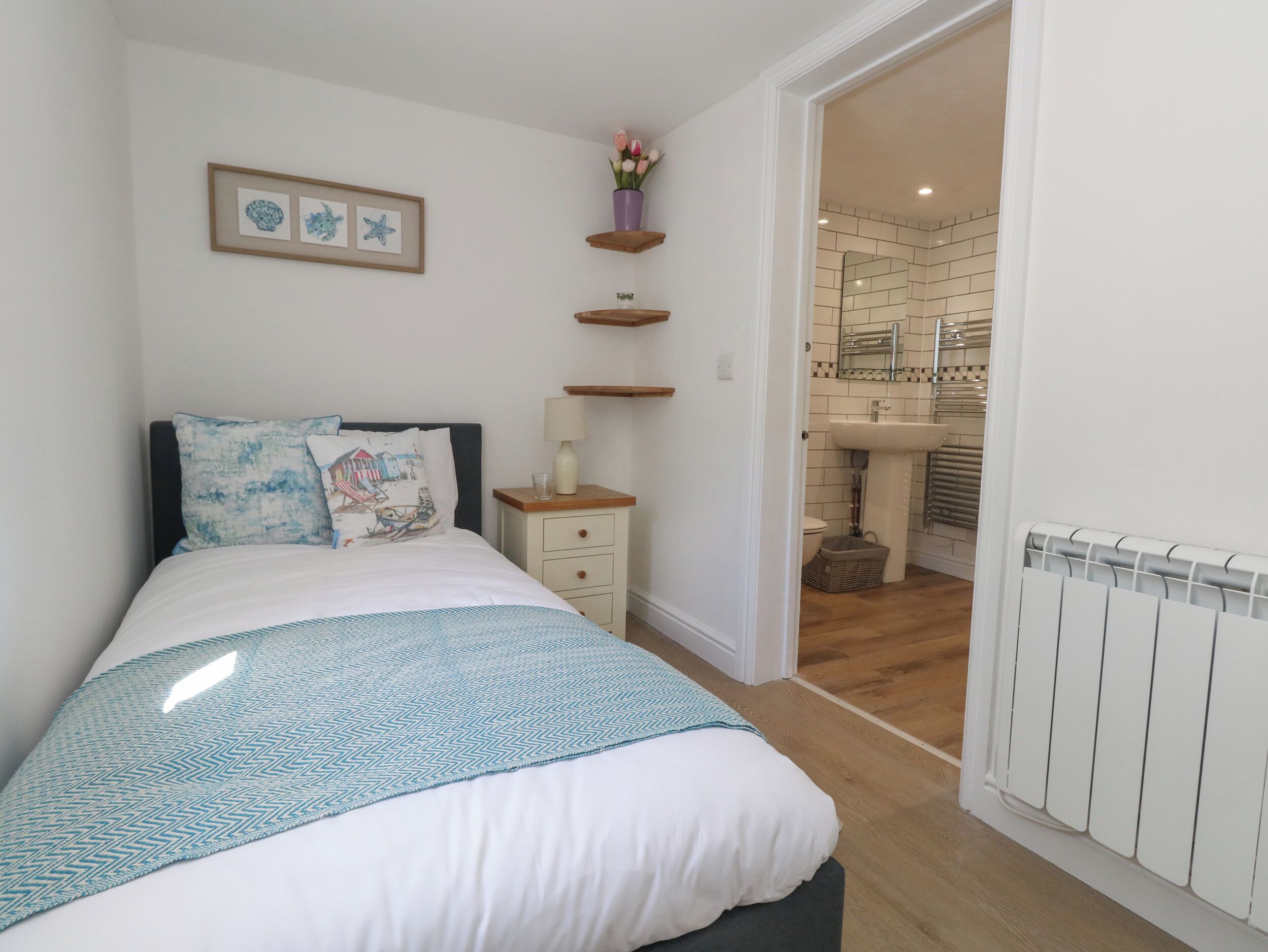 A bedroom with a bed, bedside table, lamp, and a view into the bathroom.
