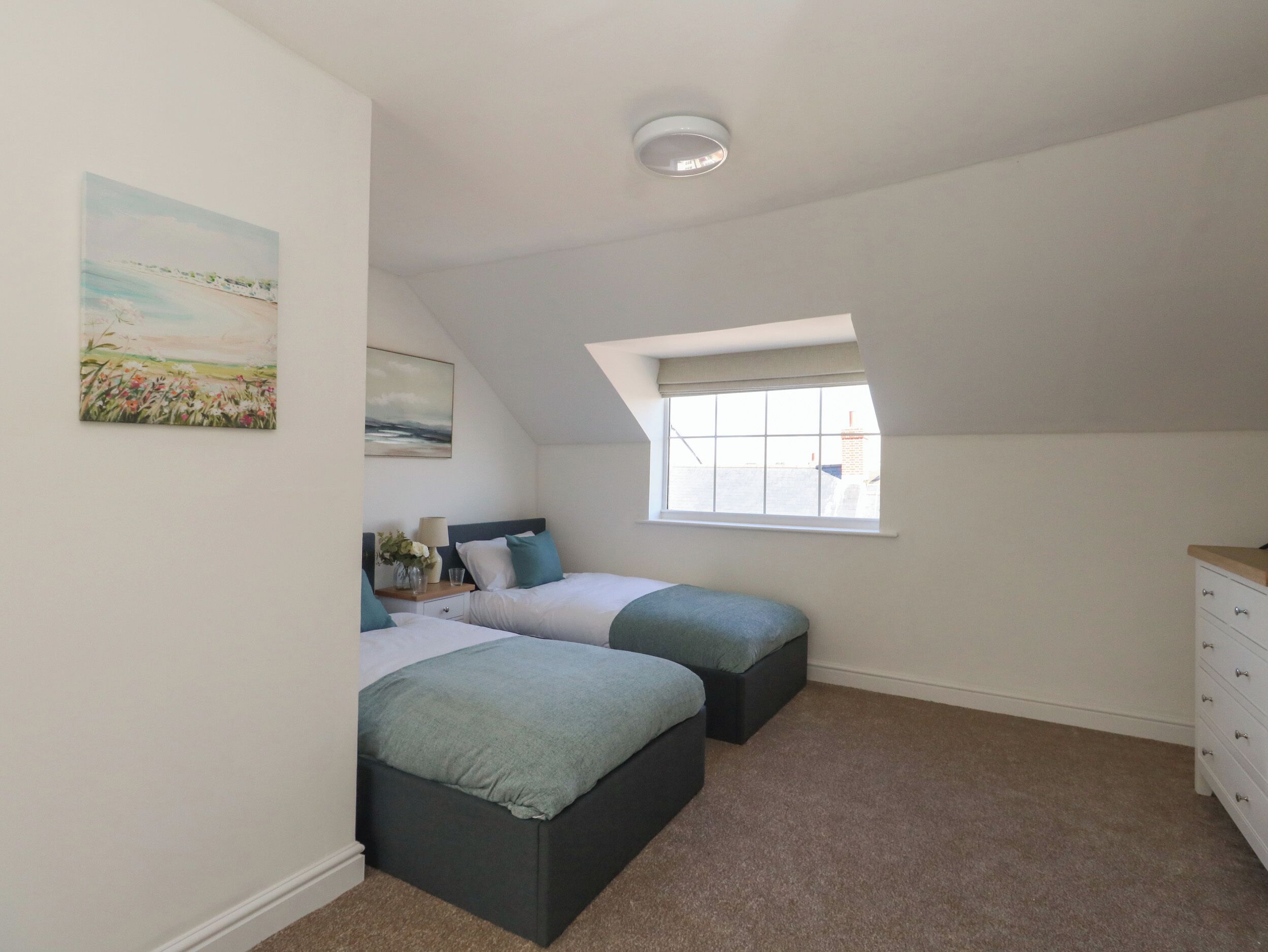 A bedroom with two beds, a window, and a ceiling light.