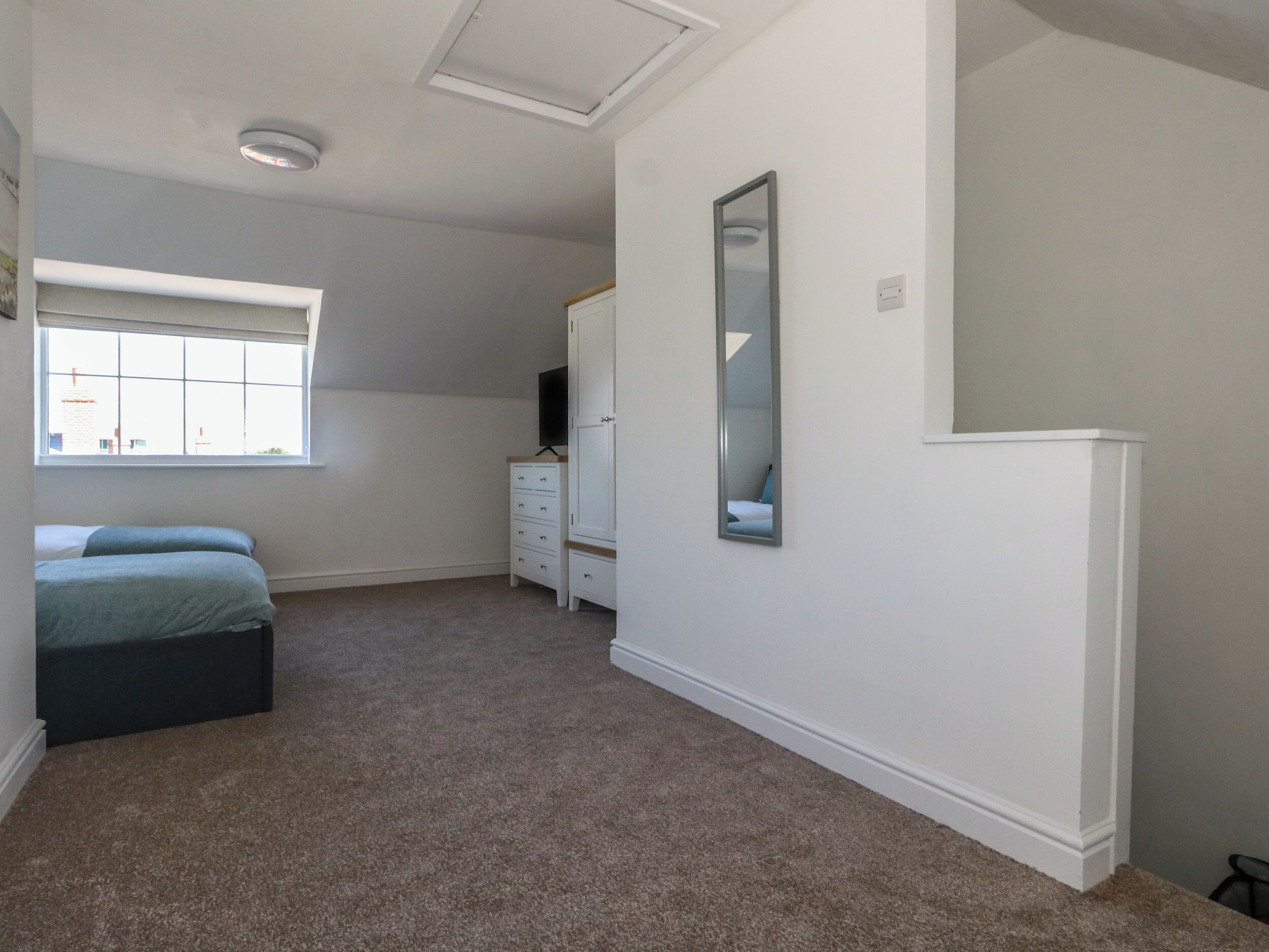 A bedroom with a large window, a bed, a dresser, a mirror, and a ceiling light.