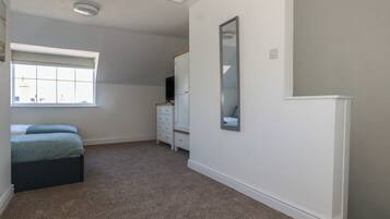 A bedroom with a large window, a bed, a dresser, a mirror, and a ceiling light.