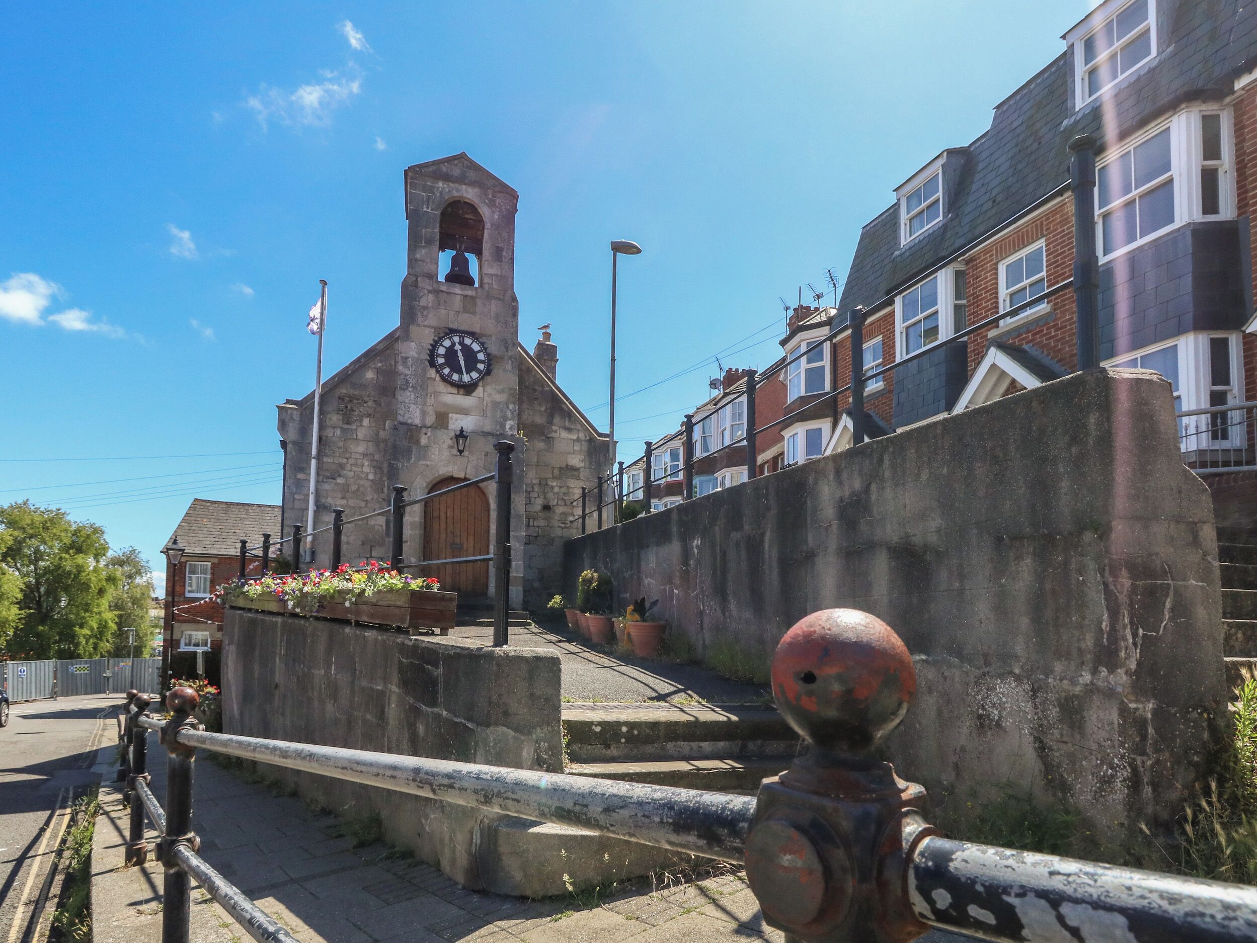 A historic building with a clock tower, a stone wall, and a metal railing.