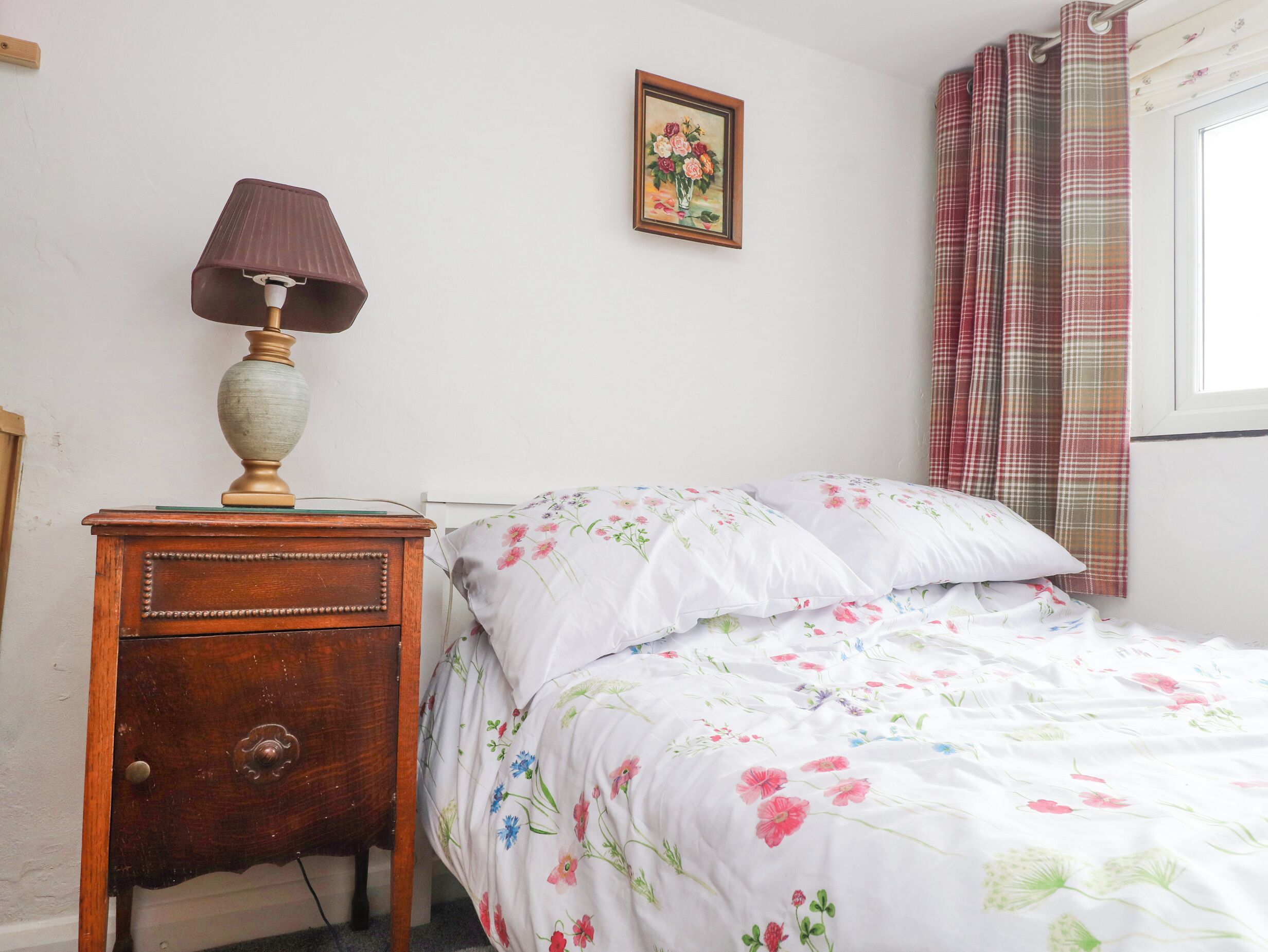 A bedroom with a bed, a nightstand, a lamp, a framed picture on the wall, and a window with curtains.