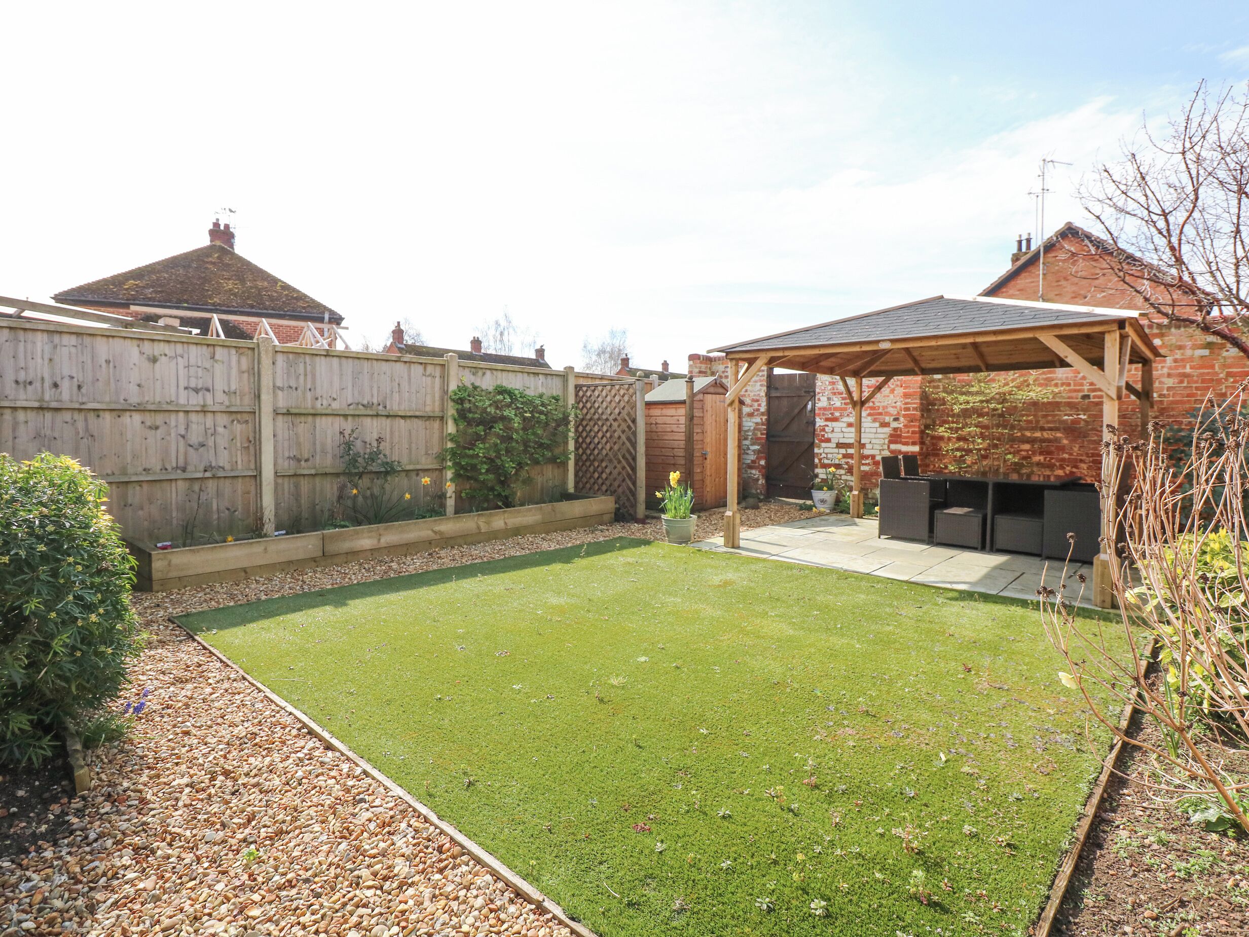 A backyard with a wooden deck, a patio area with outdoor furniture, and a brick wall.