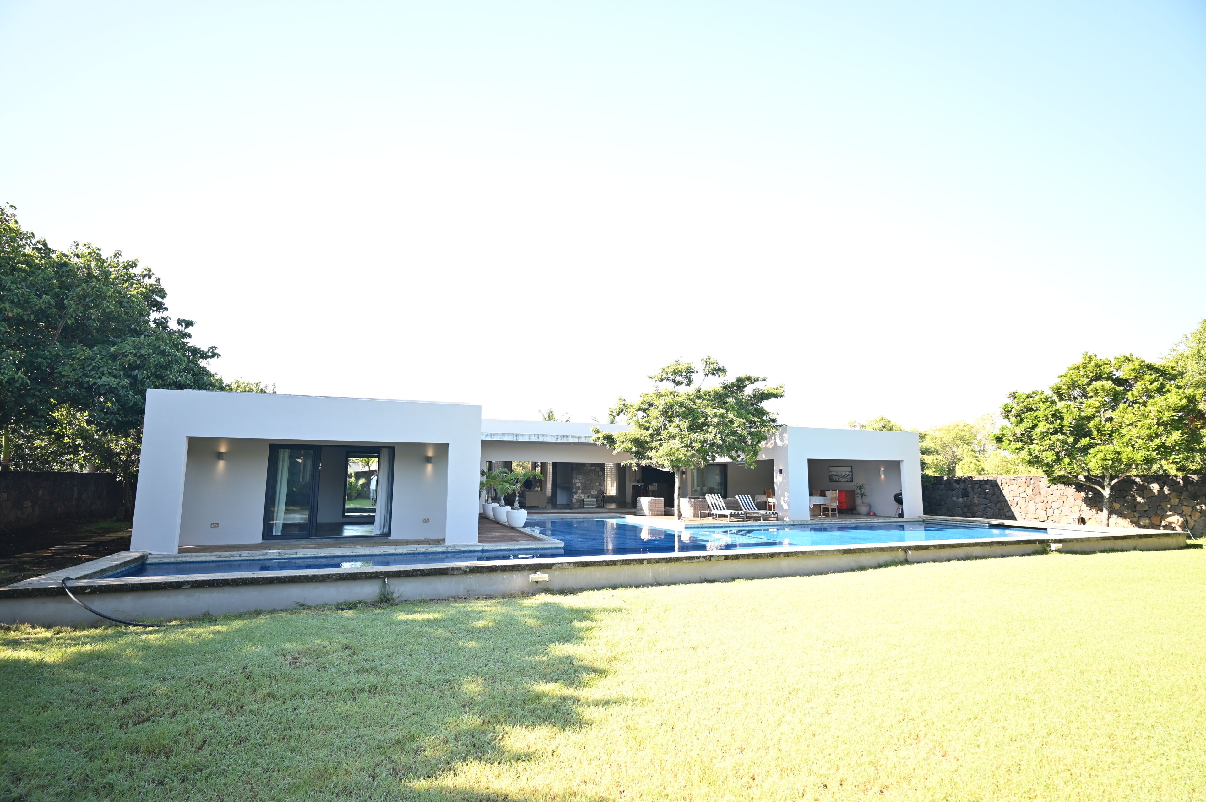 Una casa moderna con piscina, un patio cubierto y un muro de piedra.
