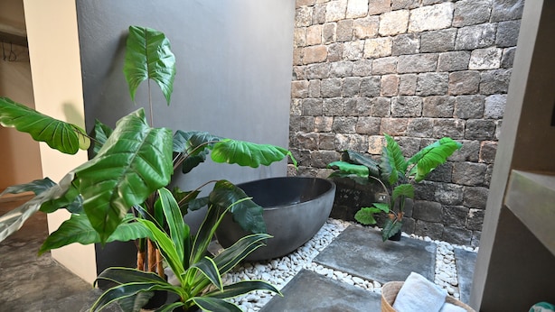 Un patio con suelo de piedra, un recipiente negro grande, plantas en macetas y una cesta de mimbre con toallas.