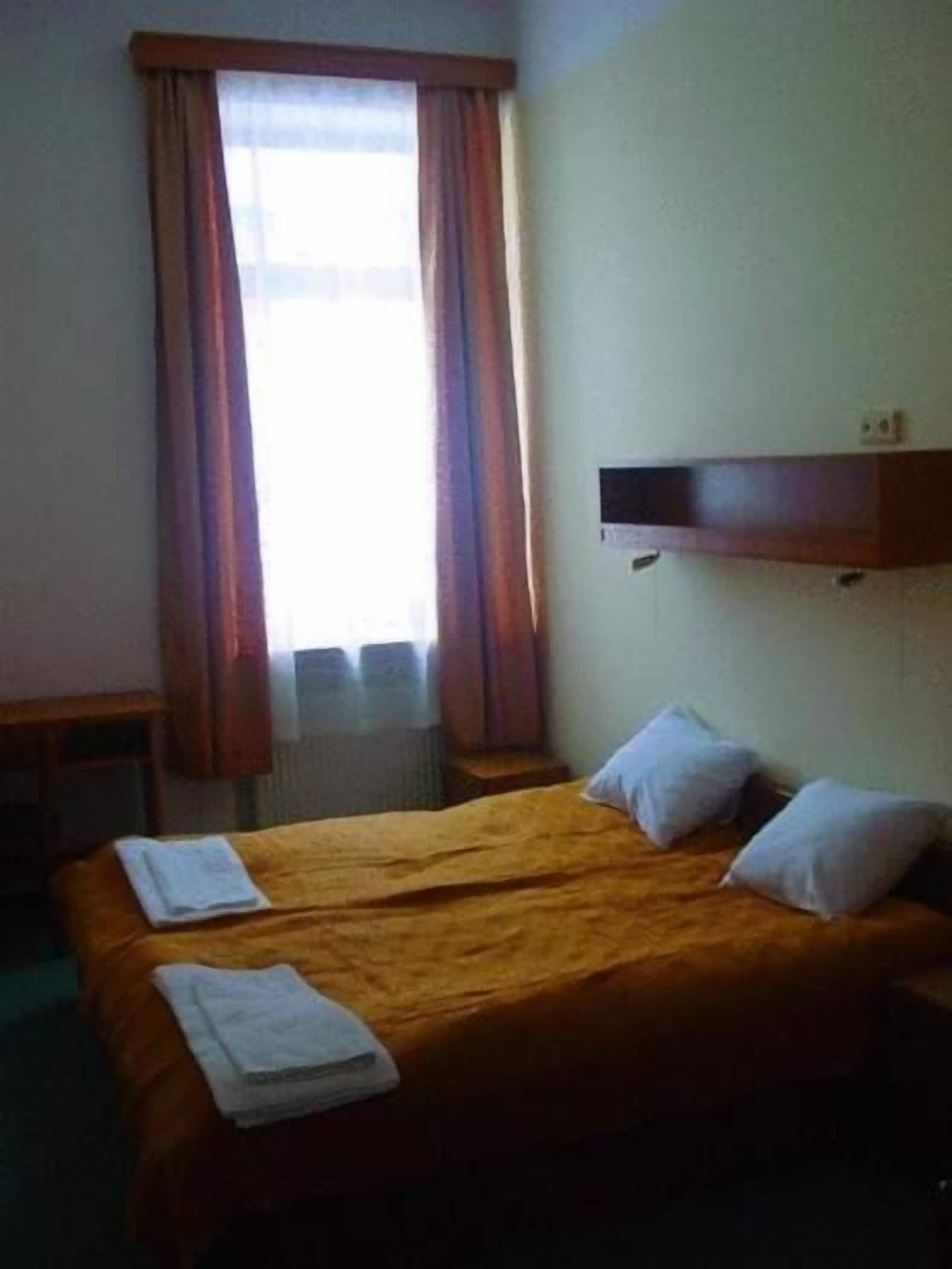 A hotel room with a double bed, two pillows, a small table, and a window with curtains.