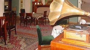 A room with a large brass gramophone, a wooden desk with a record player, a green armchair, and a patterned carpet. - HOTEL ALEF (Kraków)