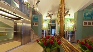 A hotel lobby with a staircase, a large mirror, and a vase of red tulips. - HOTEL ALEF (Kraków)