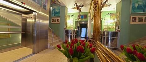 A hotel lobby with a staircase, a large mirror, and a vase of red tulips.
