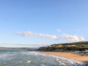 Une plage avec des vagues, des gens et un paysage vallonné en arrière-plan.