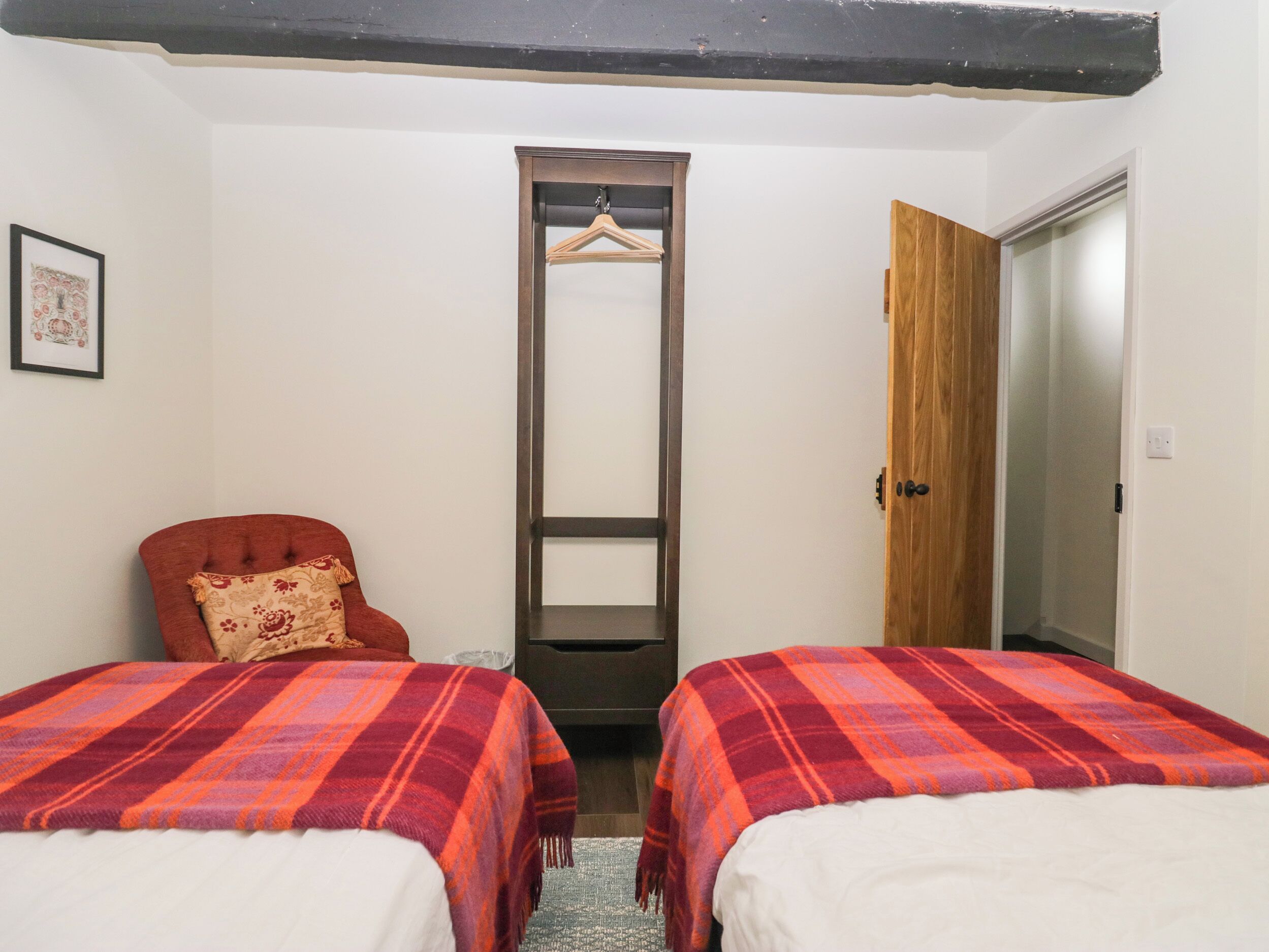 A room with two beds, a chair, a wardrobe, and a framed picture on the wall.