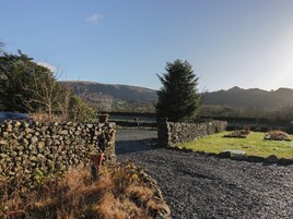 A stone wall with a potted plant, a gravel path, and a grassy area with a tree.