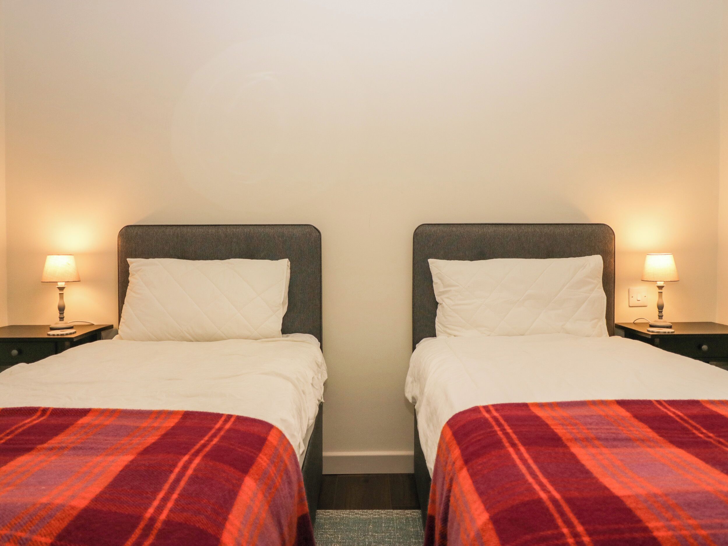 Quarto de hotel com duas camas de solteiro, cada uma com almofada e luminária na mesinha de cabeceira.