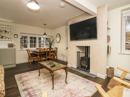 A living room with a fireplace, a dining area with a table and chairs, and a kitchen area with cabinets and a window.