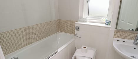 Een badkamer met een bad, toilet, wastafel en een raam.