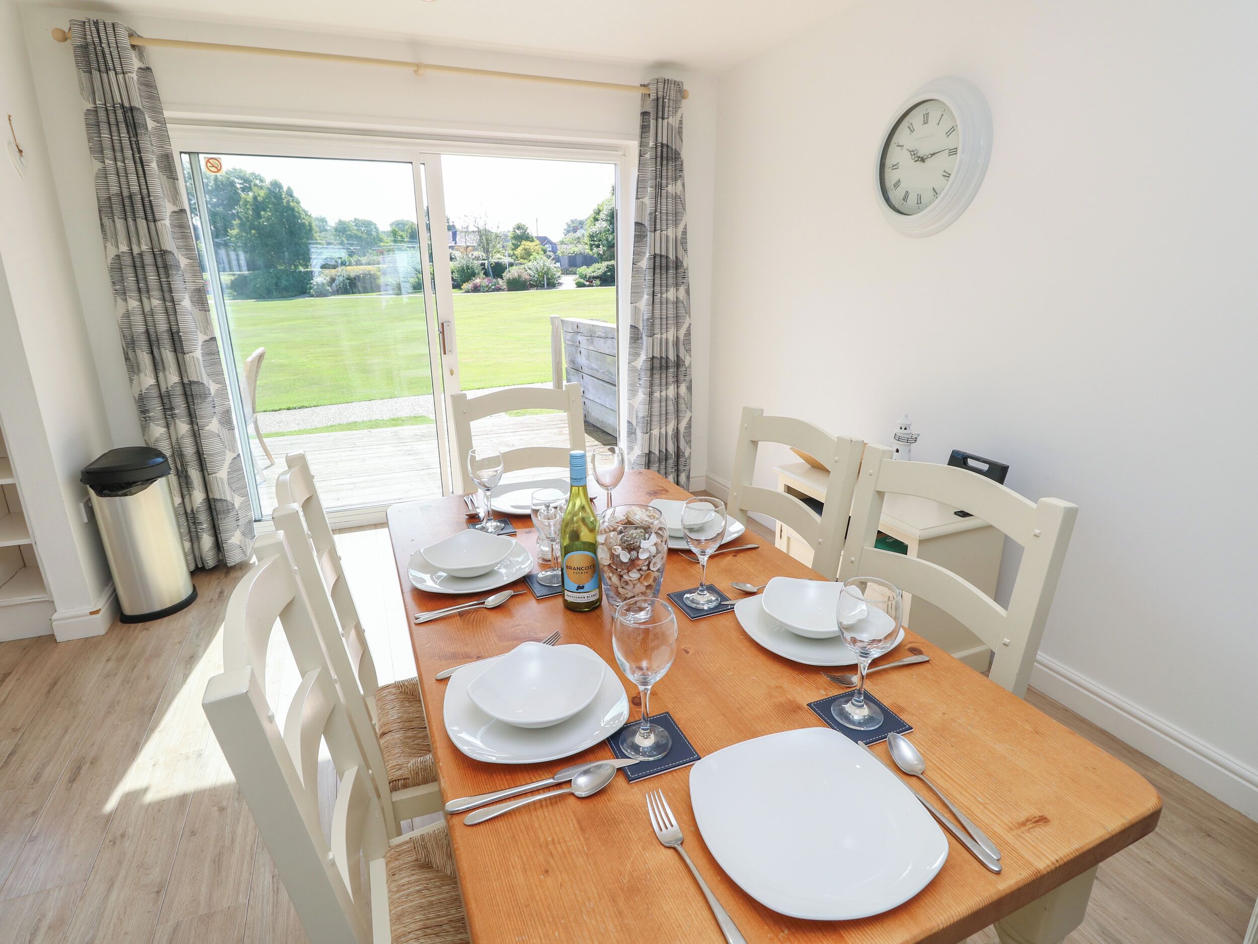 A dining area with a table set for four, a bottle of wine, and a clock on the wall.