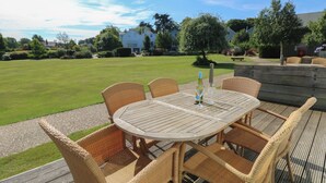 A round wooden table with wicker chairs, a bottle of wine, and two glasses on a deck. - Whitfield P5 (Yarmouth)