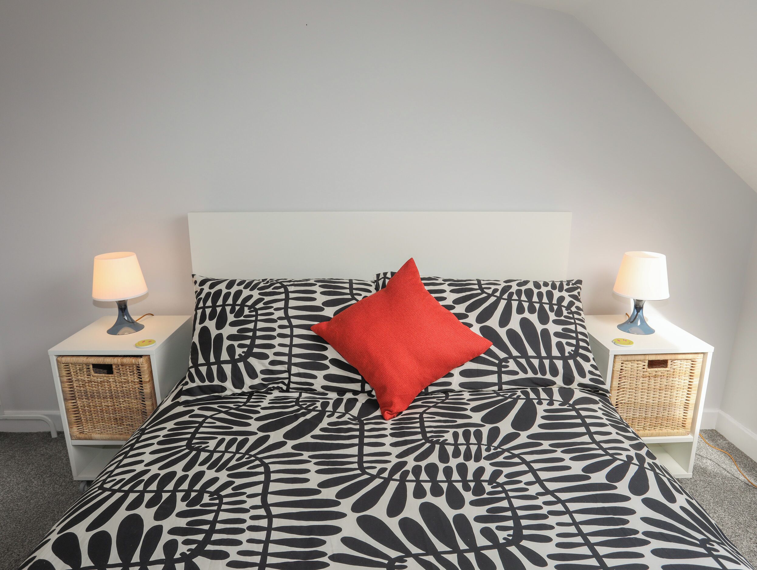 A bed with a black and white abstract pattern, a red pillow, and two bedside lamps on white nightstands.